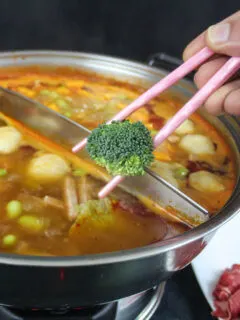 person holding broccoli in chopsticks over a pot of soup